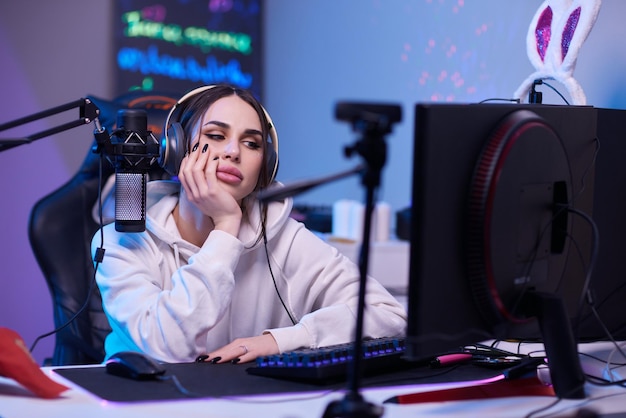 Mujer feliz poniéndose auriculares y jugando juegos de computadora Jugadora con gafas sentada y mirando el monitor de la computadora