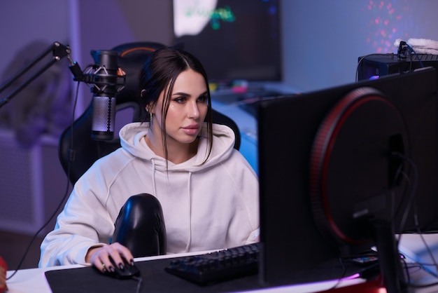 Mujer feliz poniéndose auriculares y jugando juegos de computadora Jugadora con gafas sentada y mirando el monitor de la computadora
