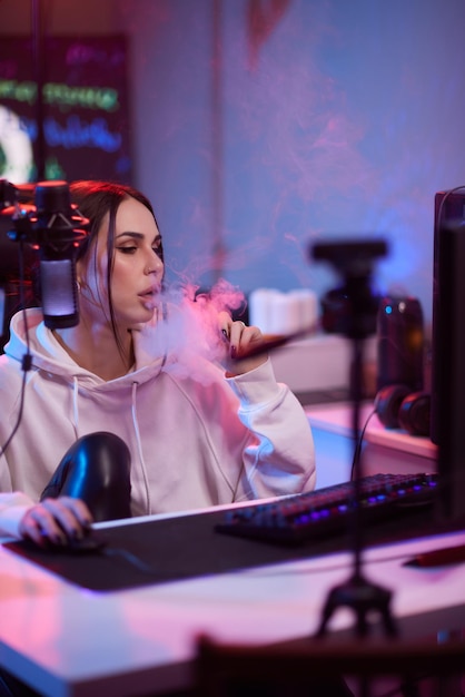 Mujer feliz poniéndose auriculares y jugando juegos de computadora Jugadora con gafas sentada y mirando el monitor de la computadora