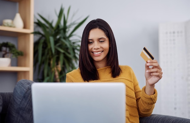 Mujer feliz portátil y sofá con tarjeta de crédito para compras en línea o compras en casa Mujer joven o compradora con sonrisa para pagos remotos comercio electrónico o fintech en el sofá en casa