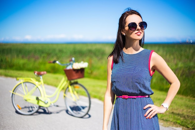 Foto mujer feliz posando en la carretera con una bicicleta retro