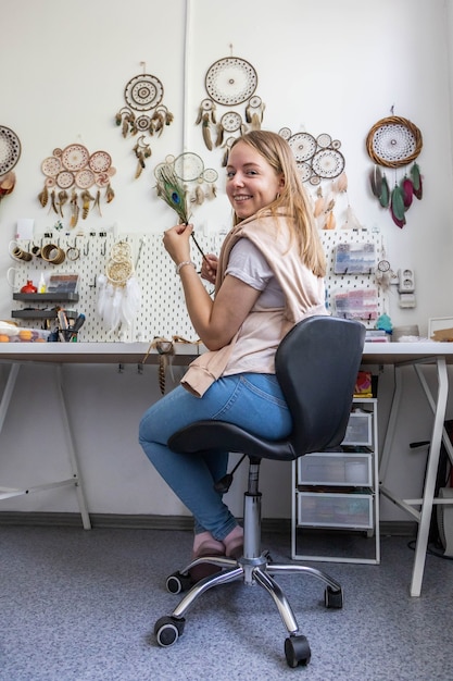 Mujer feliz posando con pluma de pavo real en el taller de creación de atrapasueños utiliza material natural