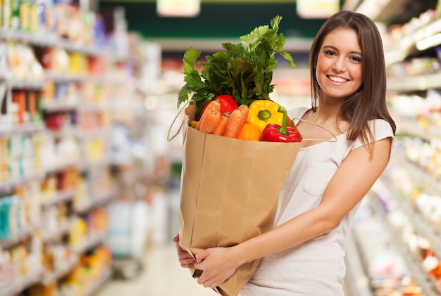 Mujer feliz positiva saludable sosteniendo una bolsa de papel llena de frutas y verduras