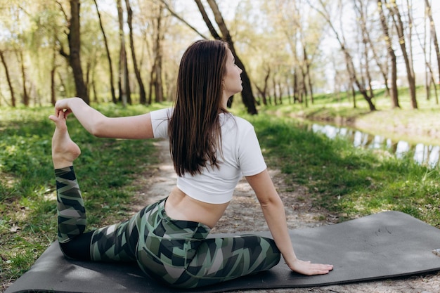 Mujer feliz practicando yoga asana pose de mariposa para aliviar la ansiedad sentada en una alfombra deportiva en la naturaleza Mujer yogui profesional sonriente haciendo ejercicio relajante descalzo al aire libre Yoga y meditación