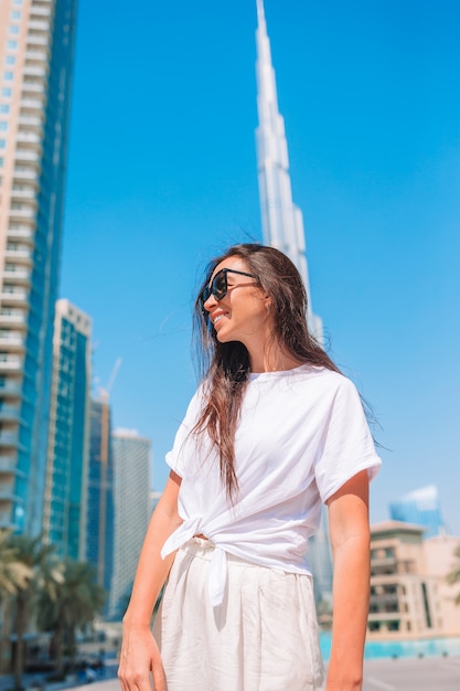 Mujer feliz que camina en Dubai con el rascacielos de Burj Khalifa en el fondo.