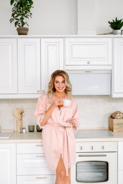 Mujer feliz que se coloca con la taza de café o de té de la mañana.