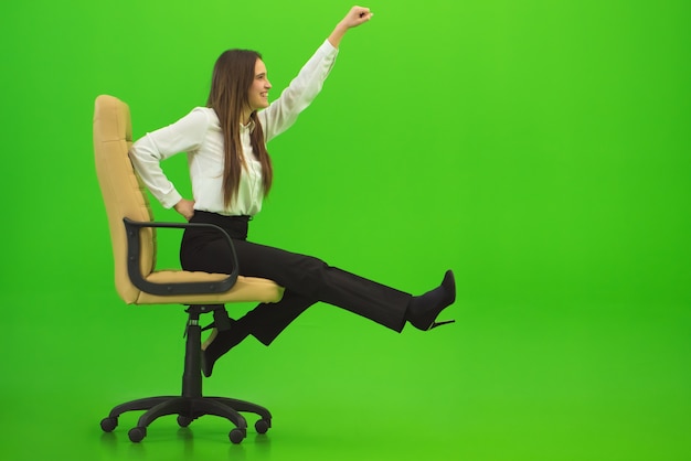 La mujer feliz que se divierte en la silla en el fondo verde