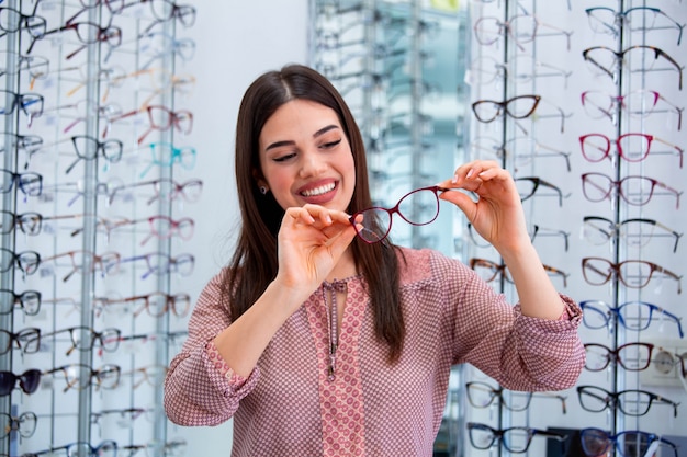 Mujer feliz que elige los vidrios en la tienda de óptica