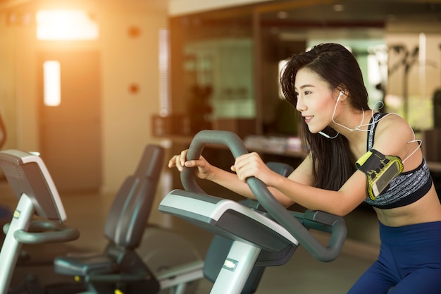 Mujer feliz que monta una bicicleta estática en gimnasio