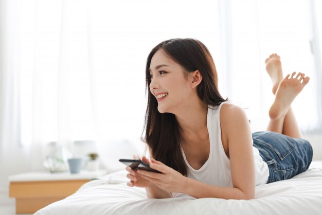 Mujer feliz que se relaja usando y hablando por teléfono inteligente en la cama en casa concepto de tecnología y comunicación.