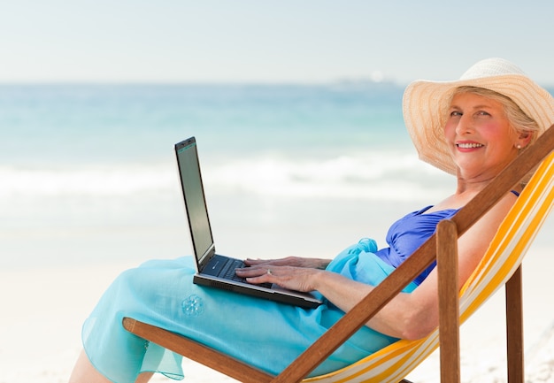 Mujer feliz que trabaja en su computadora portátil en la playa