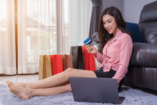 Mujer feliz que usa la computadora portátil para compras en línea con tarjeta de crédito en la sala de estar