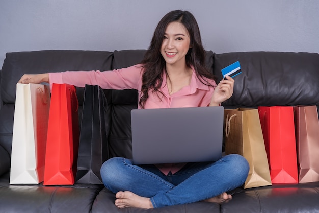 Mujer feliz que usa la computadora portátil para compras en línea con tarjeta de crédito en la sala de estar