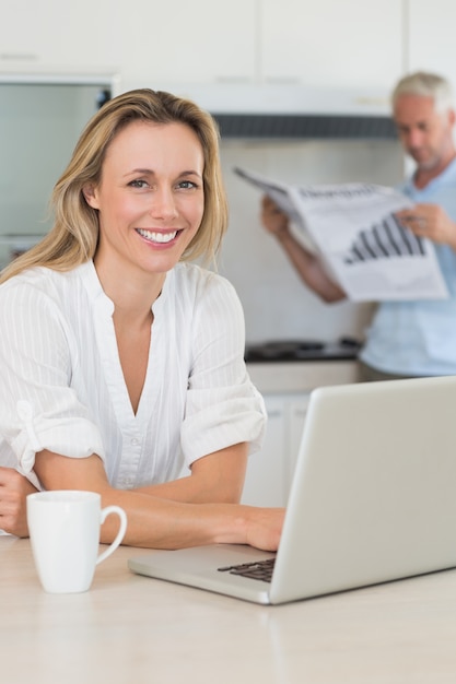 Mujer feliz que usa la computadora portátil con el socio que se coloca con el papel