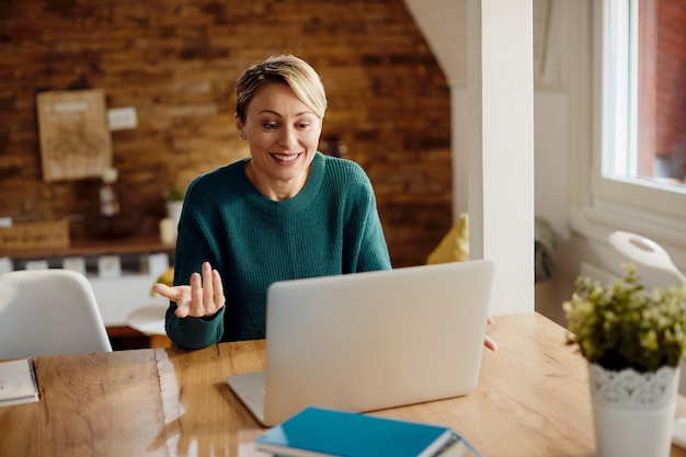 Mujer feliz que usa la computadora y tiene una llamada de conferencia desde casa