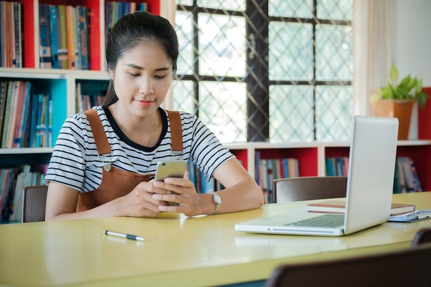 Mujer feliz que usa un teléfono elegante solo en la biblioteca.