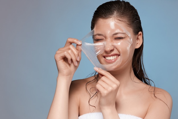 Mujer feliz quitando con dureza su mascarilla facial y sonriendo