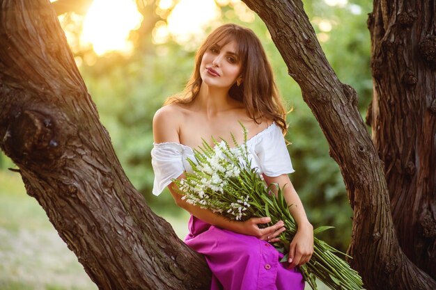 Mujer feliz con ramo de flores silvestres se ve en el lado Gran árbol viejo en el fondo