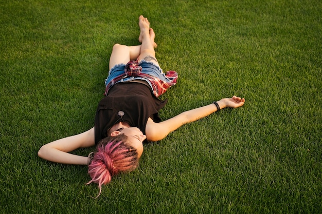 Mujer feliz con rastas rosa descansando sobre la hierba. Concepto de libertad y relajación al aire libre