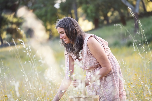 Mujer feliz recogiendo flores silvestres con cesta de mimbre