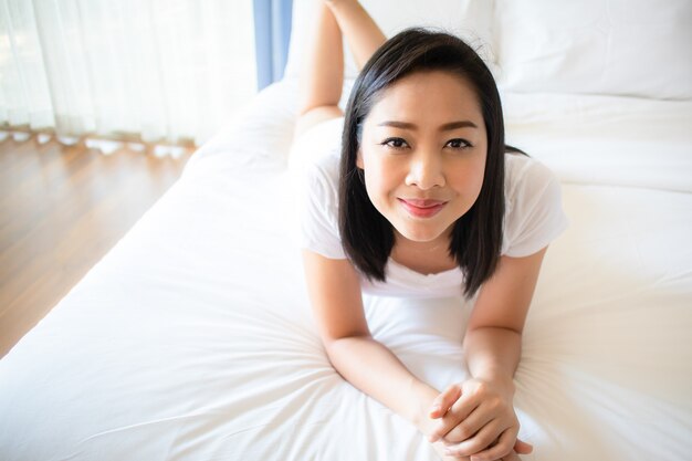 La mujer feliz se relaja en la cama con la luz de la mañana.