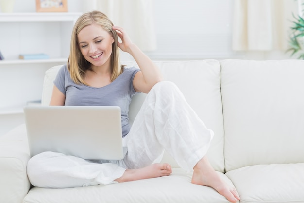 Mujer feliz relajada usando la computadora portátil en el sofá