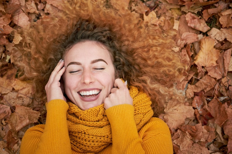 Mujer feliz rizada pelirroja liying en las hojas de otoño y sonriendo con los ojos cerrados