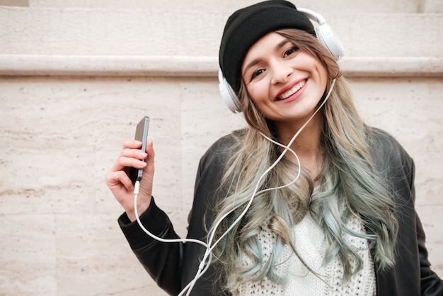 Mujer feliz en ropa de abrigo escuchando música en la calle