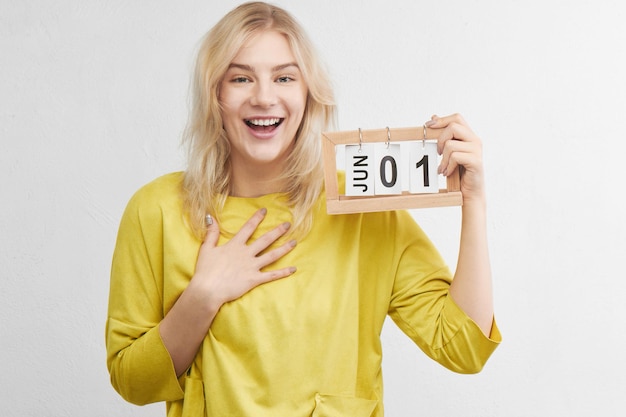 Mujer feliz con ropa amarilla sonríe, ríe y se regocija el primero de junio en el calendario de fondo blanco. Vacaciones de verano, viajes, vacaciones.