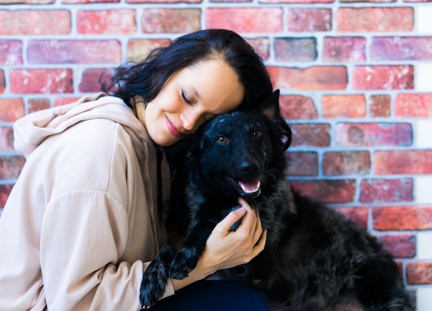 Una mujer feliz con ropa casual abrazando a un perro mascota de pura raza, Mudi, con el dueño en el fondo del estudio.