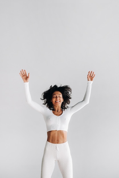 mujer feliz con ropa deportiva blanca rebota sobre un fondo blanco la niña saltando levantó las manos en el gimnasio | Foto Premium