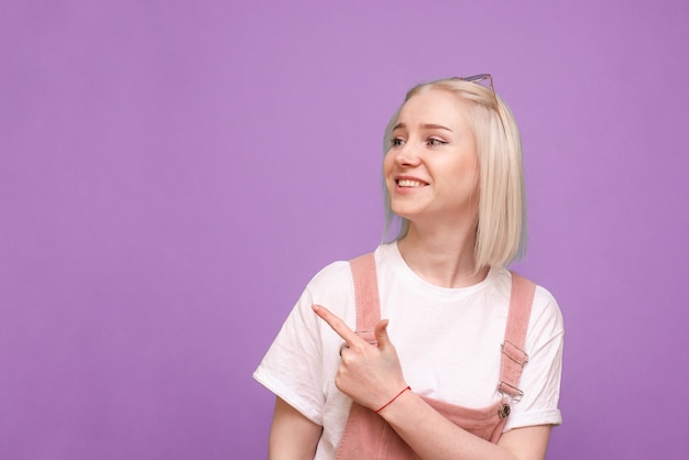 Mujer feliz en ropa linda de pie mostrando su dedo a un lado