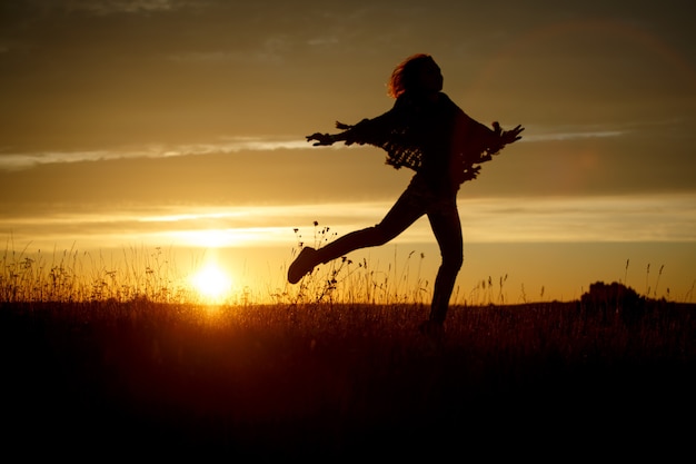 Mujer feliz saltando en el campo al atardecer