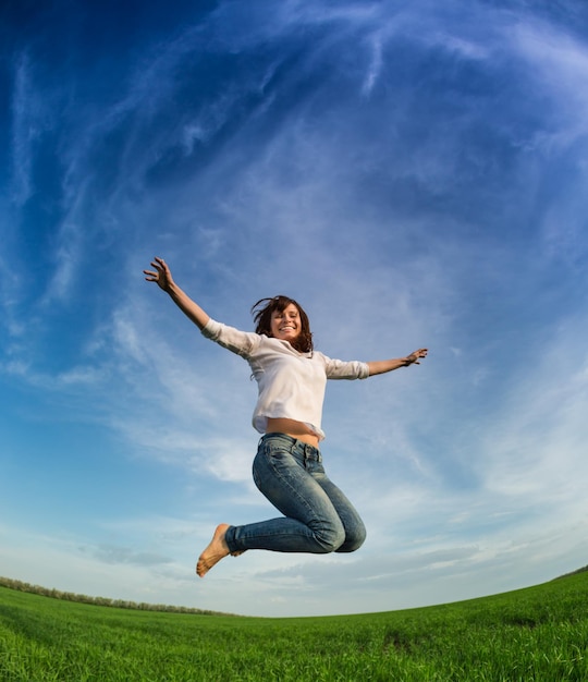 Mujer feliz saltando en campo verde contra el cielo azul Concepto de vacaciones de verano