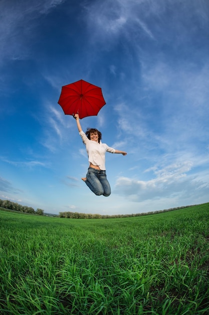 Mujer feliz saltando en campo verde contra el cielo azul Concepto de vacaciones de verano