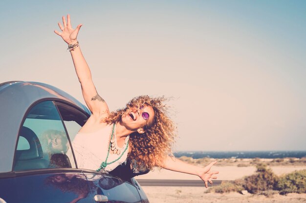 Mujer feliz saludando mientras mira desde el coche contra el cielo despejado