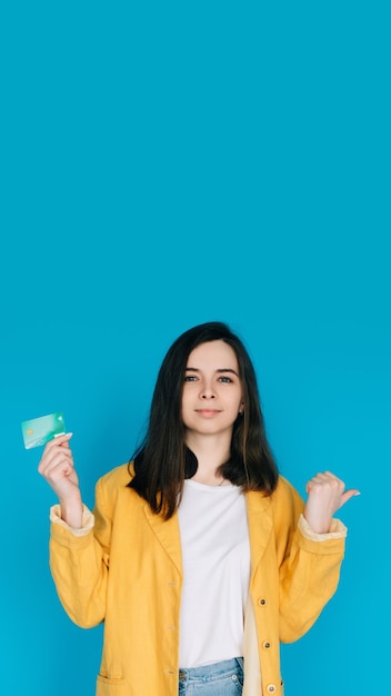 Mujer feliz señalando el pulgar en el espacio vacío con tarjeta de crédito Expressi femenino positivo y atractivo