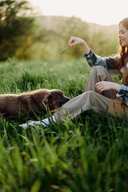 Foto mujer feliz sentada en la naturaleza y jugando con su mascota en el parque sentada en el césped verde a la luz del sol de verano por la noche jugando en la naturaleza foto de alta calidad