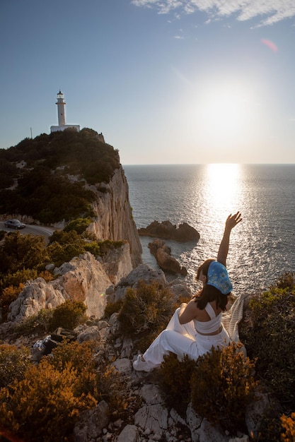 Mujer feliz sentada en la vista del acantilado vista del faro de la isla de Lefkada puesta de sol sobre el mar Grecia