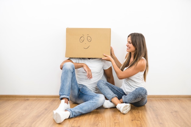 La mujer feliz se sienta cerca del hombre con una caja de cartón en la cabeza.