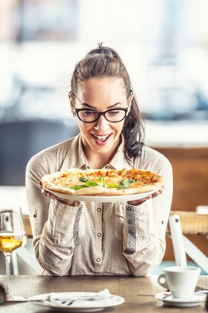 Una mujer feliz se sienta en una pizzería con una pizza fresca en las manos