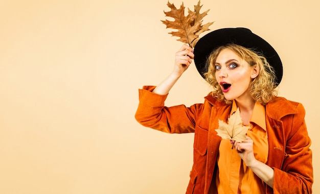 Mujer feliz con sombrero negro con hojas de otoño. Tendencias de moda para el otoño. Otoño Ropa y tendencias de color.