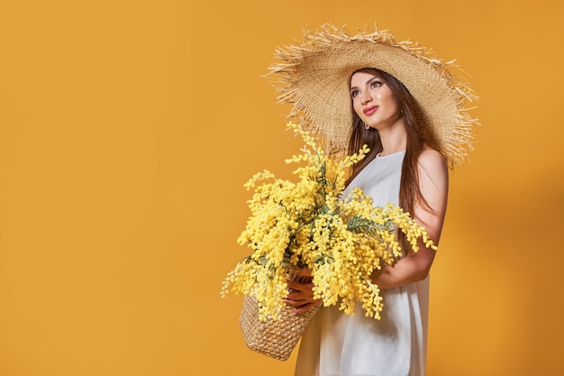 Mujer feliz en sombrero de paja de vestido blanco de verano con ramo de flores en bolsa