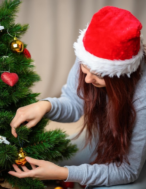 Foto mujer feliz con sombrero de santa decora el árbol de año nuevo