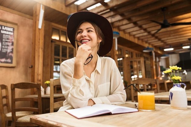 Mujer feliz con sombrero sentado en la mesa de café en el interior