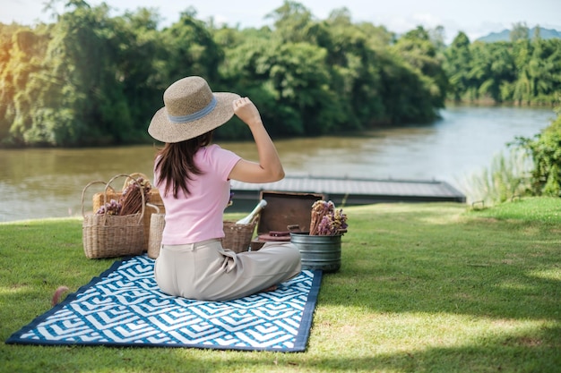 Mujer feliz con sombrero en tiempo de picnic en el parque cerca del río Concepto de primavera y vacaciones de verano