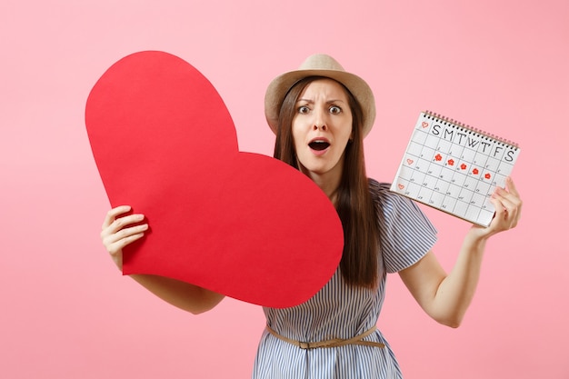 Mujer feliz con sombrero de verano vestido azul con corazón rojo grande en blanco vacío, calendario de períodos femeninos, comprobando los días de menstruación aislados en el fondo. Concepto ginecológico de atención médica. Copia espacio