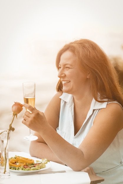 La mujer feliz sonríe levantando una copa de vino o champán en el contexto de la playa de arena.