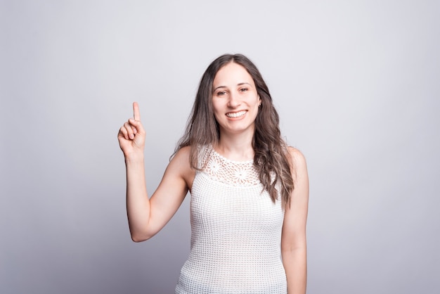 Mujer feliz sonriendo y apuntando hacia arriba en blanco.