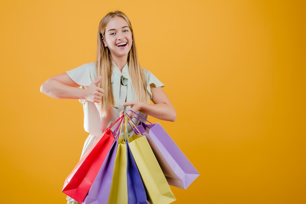 Mujer feliz sonriente que muestra los pulgares para arriba con coloridos bolsos de compras aislados sobre amarillo